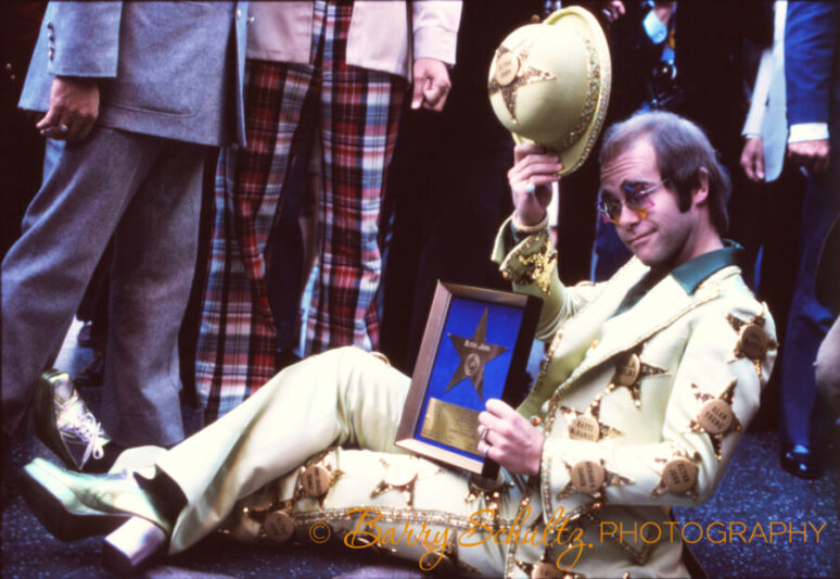 Elton John posing with his Hollywood Star on the Hollywood Boulevard Walk of Fame during the ceremony in the year 1975.