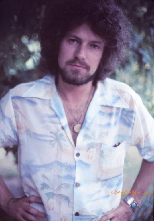 Don Henley of the Eagles sitting outside in Glenn Frey's garden in a blue, pink and white shirt.