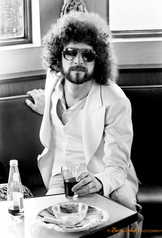 Portrait of Lindsey Buckingham of Fleetwood Mac in a white suit wearing aviators at a table during a press meeting on a cruise boat in the harbor of Rotterdam in April 1977.
