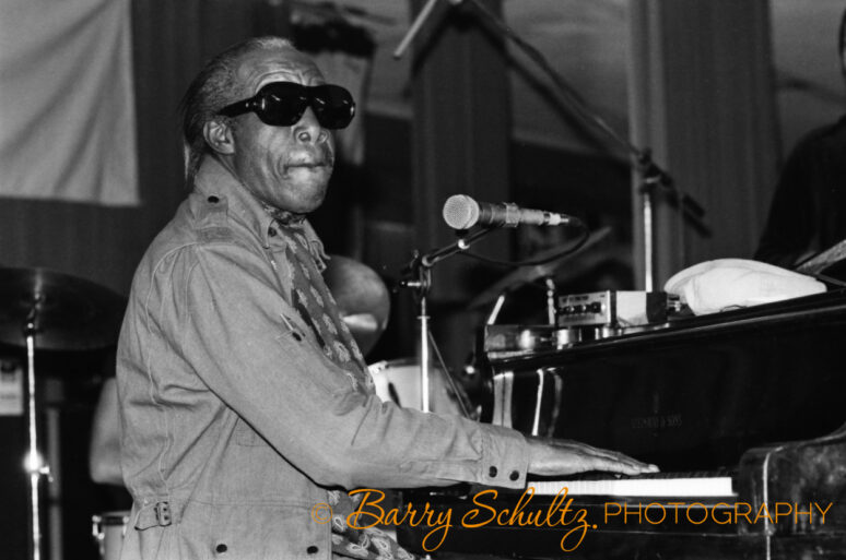 Musician Professor Longhair wearing sunglasses playing piano and singing into microphone.